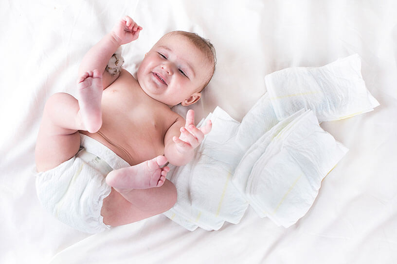 Lots of non-woven sanitary diapers lying around a playful smiling baby